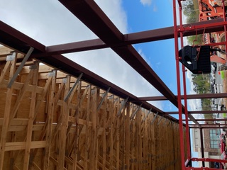 Red steel beam and joist run supporting a wood roof